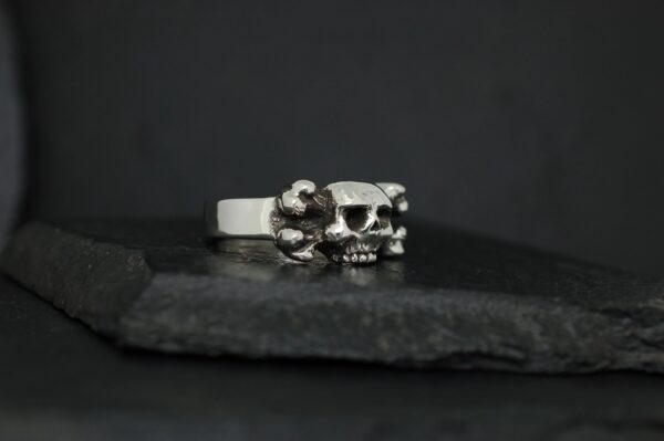 A silver ring featuring two skull designs on a dark background.