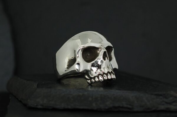 A polished silver skull ring on a dark surface.