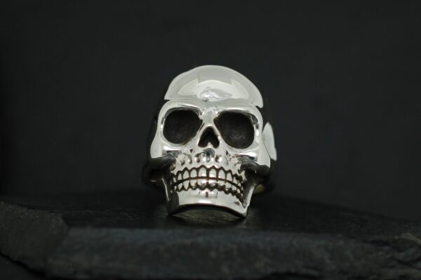 A metallic skull ring with detailed teeth and hollow eyes on a black background.