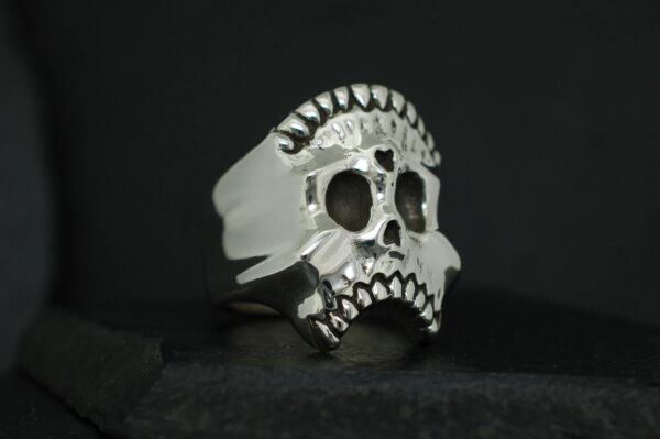 A silver skull ring with intricate detailing on a black background.