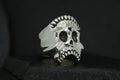 A silver skull ring with intricate detailing on a black background.