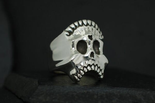 A silver skull ring with intricate detailing on a black background.