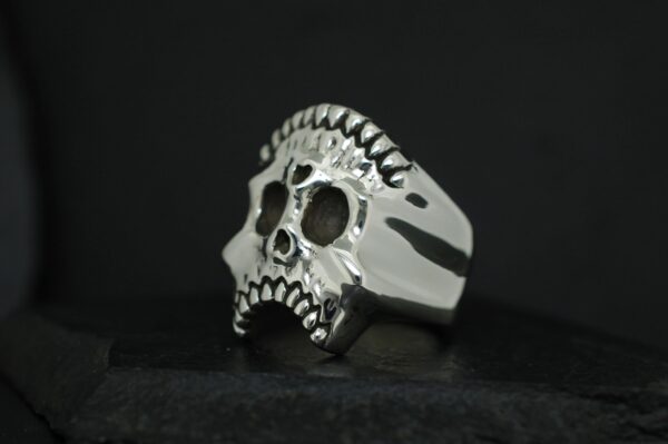 A metallic skull-shaped ring with a dark background.