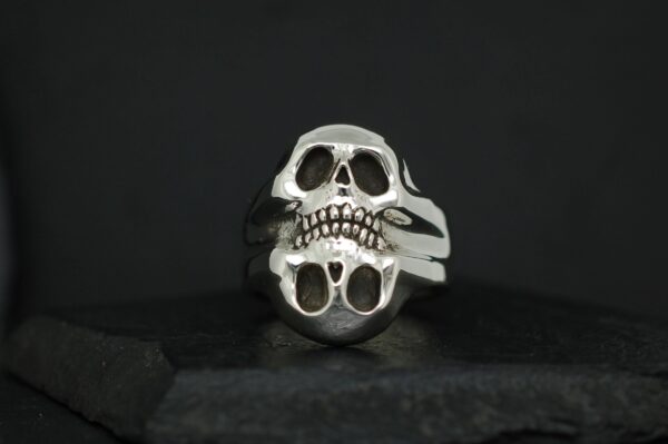 Silver skull ring with a split design against a black background.