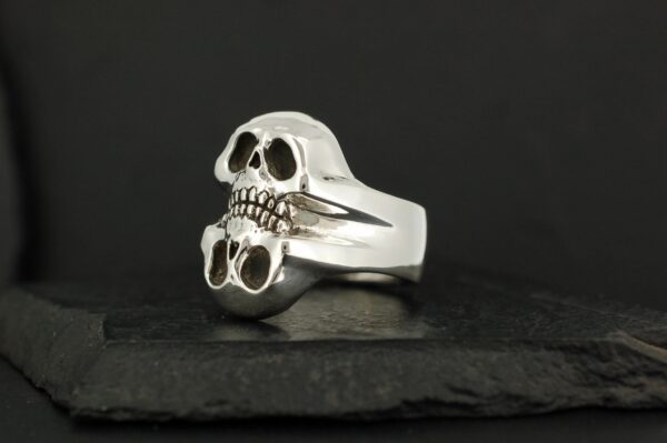 Silver skull ring with a fierce expression on a dark surface.