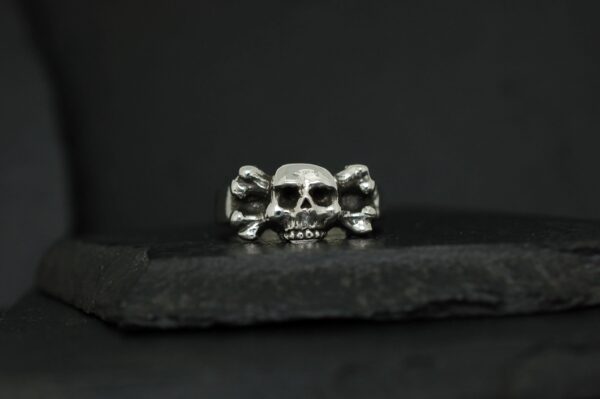 A silver ring with three detailed skulls on a dark surface.