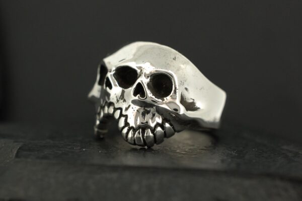 A silver ring designed as a skull with detailed teeth and eye sockets.