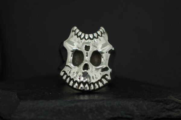 A stylized skull sculpture with exaggerated teeth and hollow eyes on a black background.