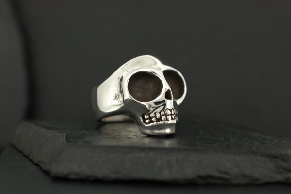 A silver skull-shaped ring on a dark surface.