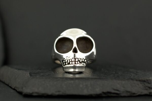 A silver skull ring with dark hollow eyes on a black surface.