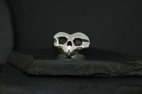 Metal skull-shaped ring on dark surface.