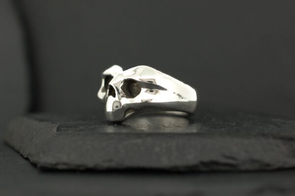 Silver skull-shaped ring on a black surface.