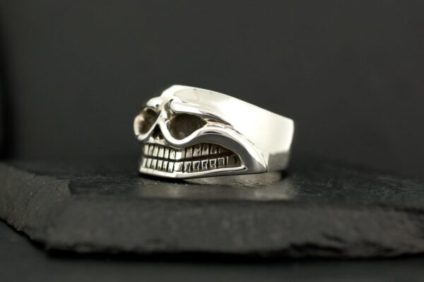 Silver skull-shaped ring with detailed teeth on a black surface.