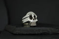 A skull-shaped ring with long eyelashes on a dark surface.