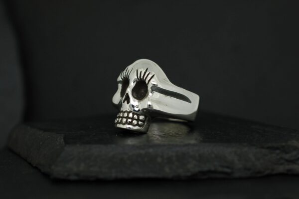 A silver skull ring with detailed engravings on a dark background.