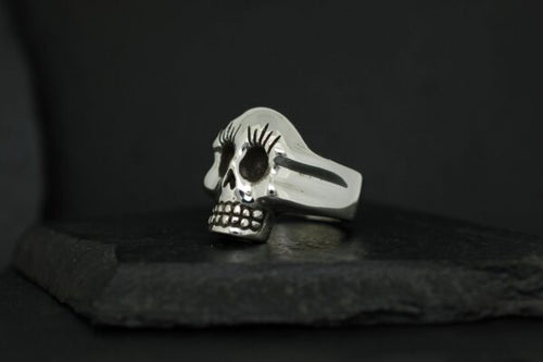 A silver skull ring with detailed engravings on a dark background.