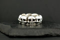 Silver ring featuring a row of detailed skulls on a dark background.