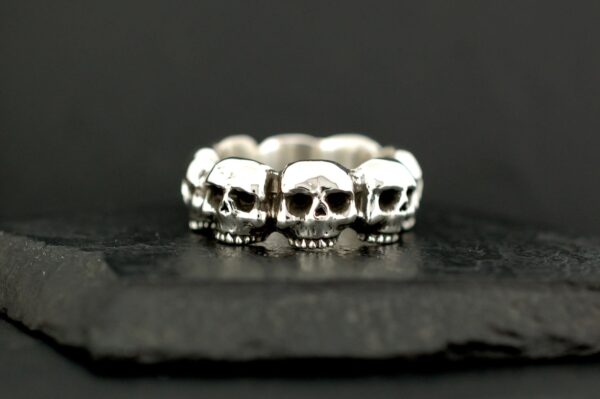Silver ring featuring a row of detailed skulls on a dark background.