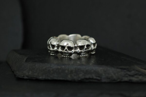 Silver ring featuring a row of detailed skulls on a dark background.