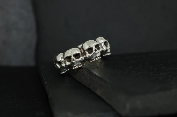 Silver ring featuring a row of skulls on a dark background.