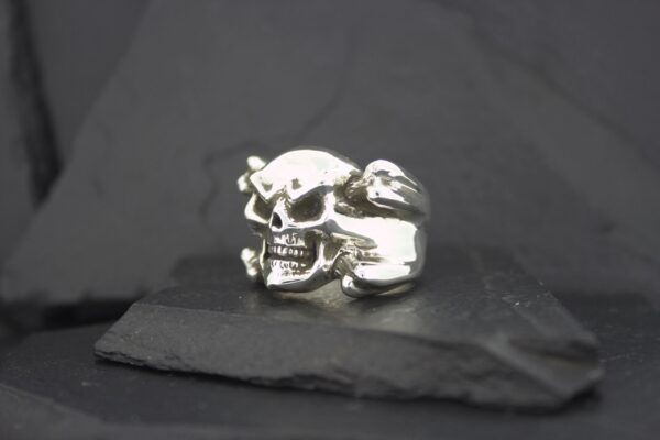 Silver skull-shaped ring on a dark surface.
