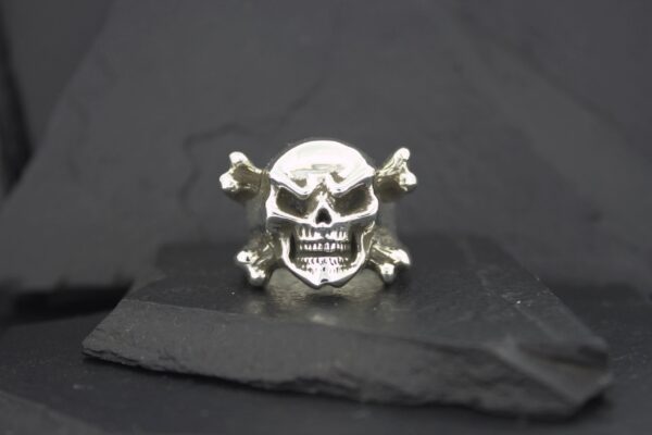 A silver skull and crossbones ring on a dark surface.