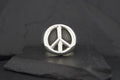 Silver peace symbol pin on a dark surface.