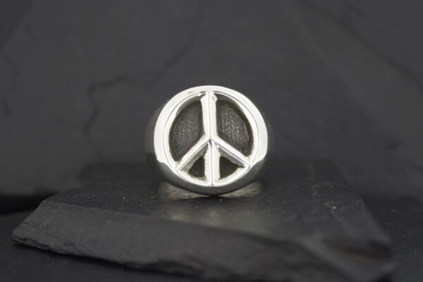 Silver peace symbol pin on a dark surface.