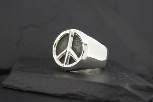 Silver ring featuring a peace symbol on a black surface.