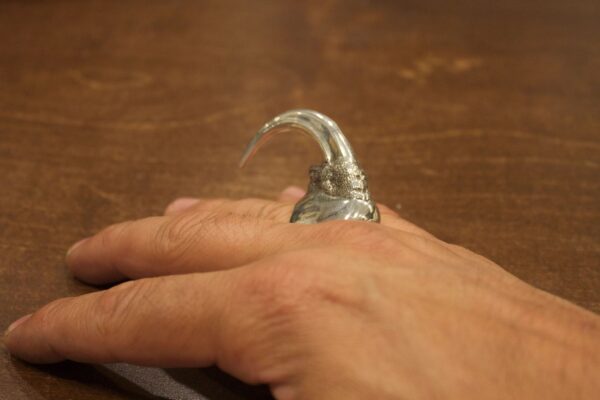 A silver claw ring worn on a finger.