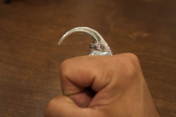 Hand with a curved, sharp metallic claw attached to the finger.