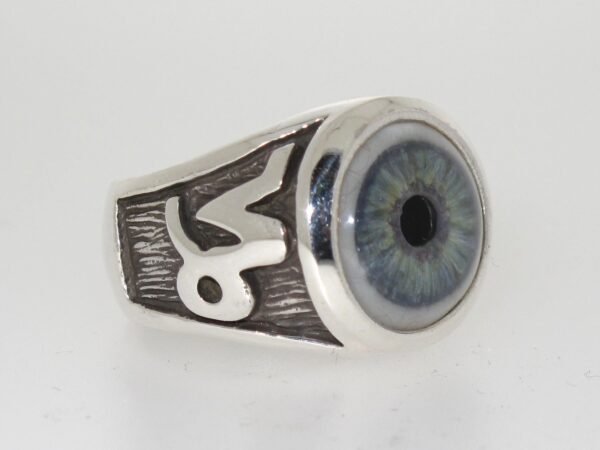 A silver ring with a detailed blue eye design and an engraved symbol.
