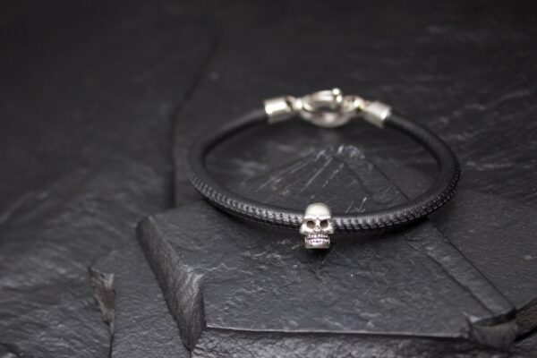 Black bracelet with a silver skull charm on a dark stone surface.