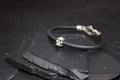 Black leather bracelet with a small silver skull charm on a slate surface.