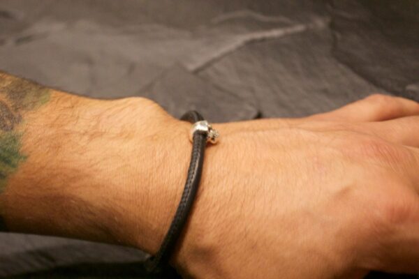 Close-up of a wrist wearing a simple black cord bracelet with a metallic bead.