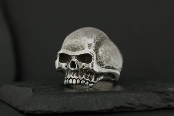Metal skull ring with detailed features on a black background.