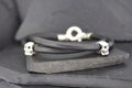 Black leather bracelet with silver skull accents on a dark slate background.