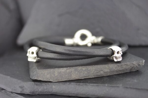 Black leather bracelet with silver skull accents on a dark slate background.