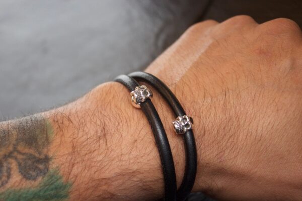 Close-up of a wrist wearing a black leather bracelet with skull charms.
