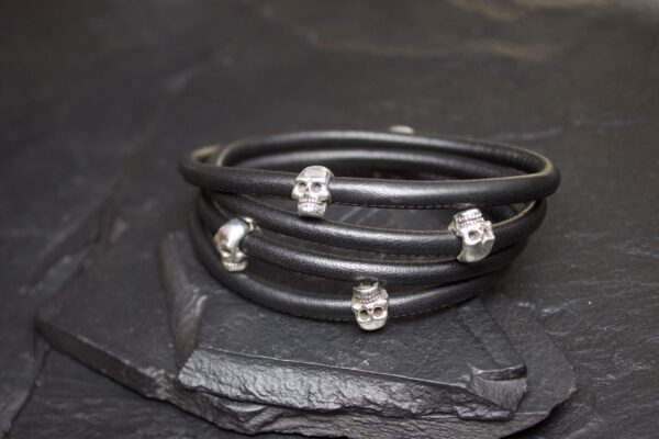 Black leather bracelet adorned with small silver skull charms.