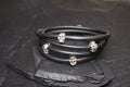 Black leather bracelet adorned with small silver skull charms.