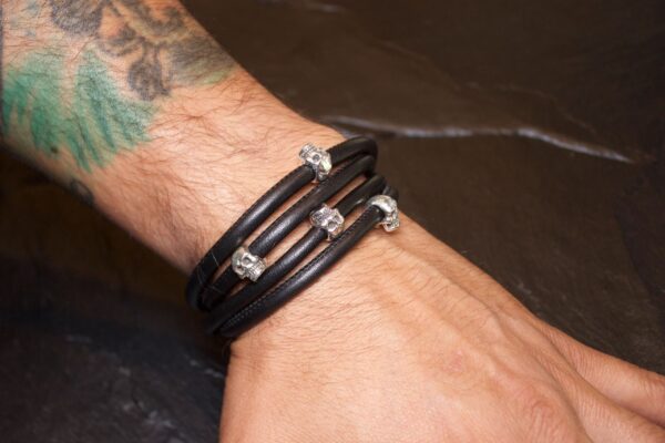 Black leather bracelet with silver accents worn on a wrist.
