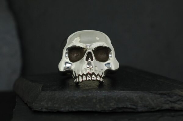 A shiny silver skull ring on a dark surface.