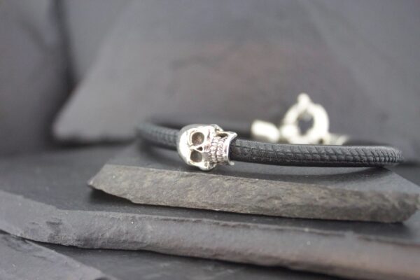 Close-up of a black bracelet with a silver skull charm on a slate surface.