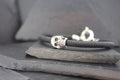 Close-up of a black bracelet with a silver skull charm on a slate surface.