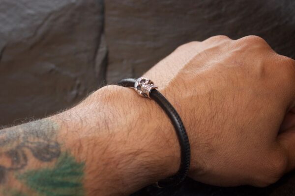 A wrist wearing a black leather bracelet with a metallic skull bead.