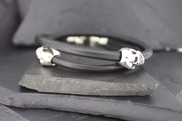 Black bracelet with silver skull accents on a dark background.