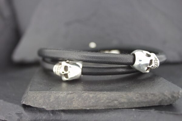 Black leather bracelet with silver skull accents on dark surface.