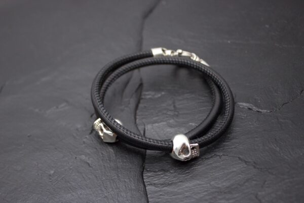 Black leather bracelet with silver skull charms on a dark surface.