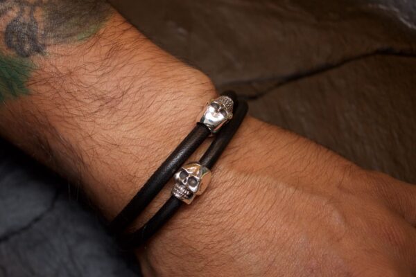 Black leather bracelet with silver skulls on a wrist.